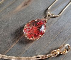 a necklace with a red glass pendant hanging from it's side on a wooden surface