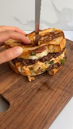 a person cutting into a sandwich with a knife on a cutting board in front of them