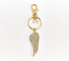 a gold key chain with an angel wing charm attached to it's side, on a white background