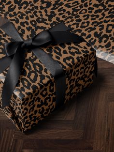 a leopard print gift box with a black bow on it's side, sitting on a wood floor