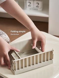 a child's hand reaching into a plastic container on top of a white table