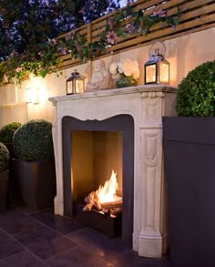 an outdoor fireplace with potted plants and lights on the top, next to it