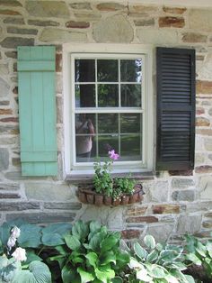 a window with shutters and potted plants in front of it on a stone house