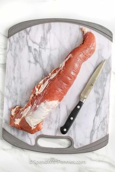 a piece of meat sitting on top of a marble cutting board next to a knife