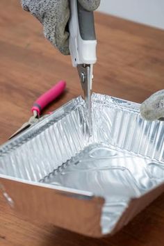 someone using a pair of scissors to cut aluminum foil on a table with a pink object in the background