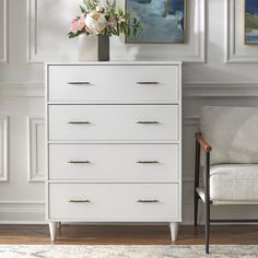 a white dresser sitting next to a chair in a living room with paintings on the wall