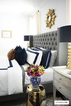 a bedroom with white and blue bedding, black and white pillows, gold accents