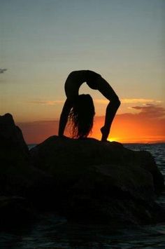 a woman doing yoga on top of a rock near the ocean at sunset or dawn