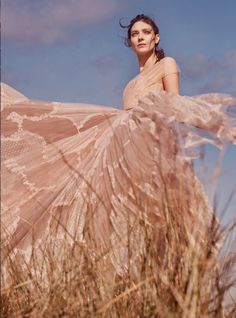 a woman in a long dress is standing among tall grass