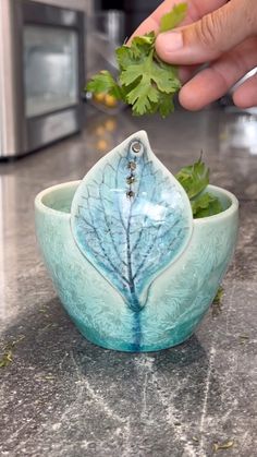 a person is picking up some leaves from a plant in a bowl on the counter