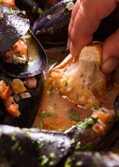 a person dipping some food into a bowl filled with mussels and other foods