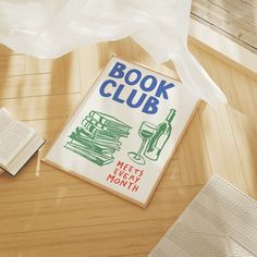 a book club sign sitting on top of a wooden floor next to an open book