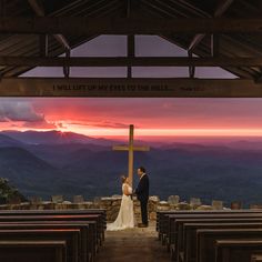 a bride and groom standing in front of a cross at sunset