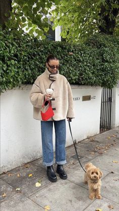 a woman walking her dog on a leash while holding a coffee cup in her hand