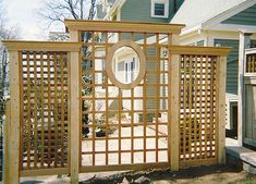 a wooden trellis with a circular mirror on it's center piece in front of a house