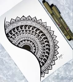 a black and white drawing of a paisley design on paper next to two marker pens