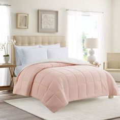 a bed with pink comforter and pillows in a bedroom