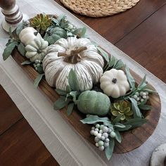 a table topped with white pumpkins and greenery on top of a wooden board