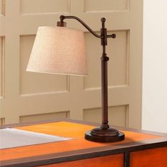 a lamp on top of a wooden desk next to a door with a white linen shade