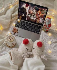 two stuffed animals laying on top of a bed next to a laptop computer and cupcakes