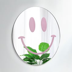 a round mirror with a smiley face painted on it's side and a plant in the middle