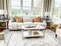 a living room filled with lots of furniture next to two lamps and large windows in the background