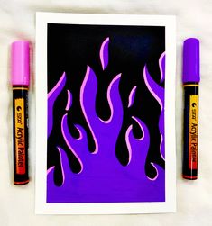 two pens are sitting next to an art print with purple flames on it and black background