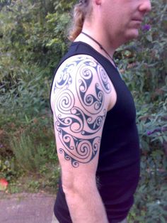 a man with a black and white tattoo on his arm standing in front of some bushes