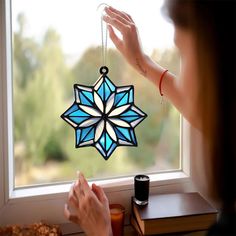 a woman is looking out the window with a stained glass snowflake ornament