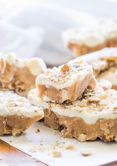 several pieces of dessert sitting on top of a cutting board with white frosting and chopped walnuts