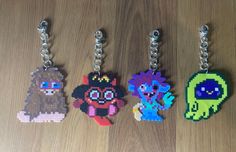 four pixel keychains are shown on a wooden surface, one has an animal and the other is a dog