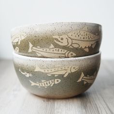 two bowls with fish painted on them sitting on a wooden table next to each other