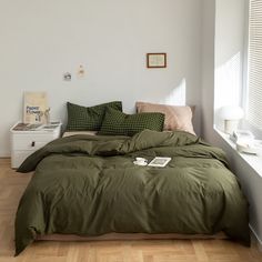 a bed with green sheets and pillows in a white room next to a wooden floor