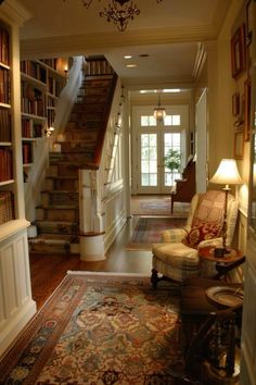 a living room filled with lots of furniture and bookshelves next to a stair case