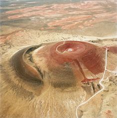 an aerial view of a red crater in the middle of nowhere, looking down on it