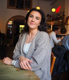 a woman sitting at a table with her arms crossed and smiling for the camera, in a restaurant