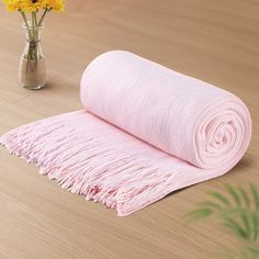 a pink blanket sitting on top of a wooden floor next to a vase with yellow flowers