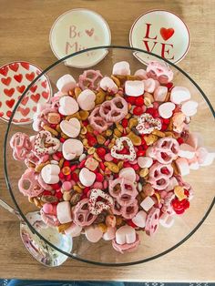 a glass bowl filled with valentine's day treats on top of a wooden table