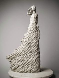 a white sculpture is standing on top of a table and it looks like a woman's dress