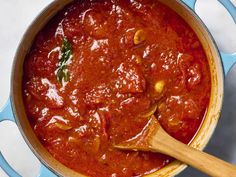 a blue pot filled with red sauce on top of a white counter next to a wooden spoon