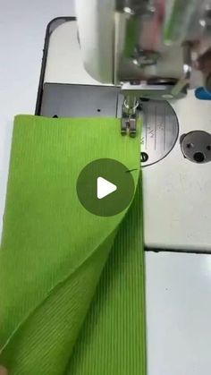 someone is using a sewing machine to sew on green fabric with the help of a pair of scissors