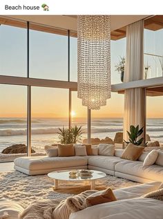 a living room filled with lots of furniture and large windows next to the ocean at sunset