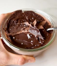 a hand holding a glass jar filled with chocolate ice cream and chunks of marshmallows