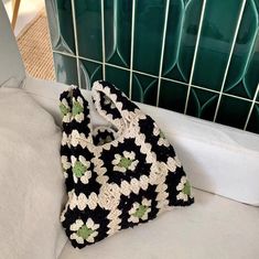 a black and white crocheted bag sitting on top of a bed next to a green tiled wall