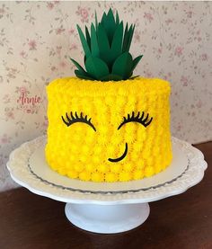 a yellow cake with a pineapple on top and eyes drawn on the side, sitting on a white pedestal