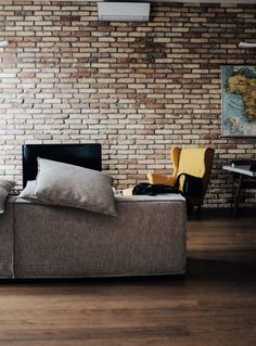 a couch with two pillows on it in front of a brick wall and wooden floor