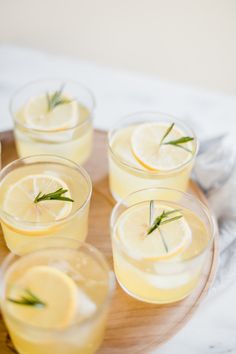 four glasses filled with lemonade and rosemary garnish on a wooden platter