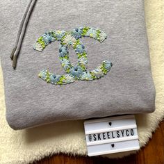 a gray sweatshirt with a flowered monogram on it and a tag hanging from the front