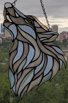 a stained glass wolf head hanging from a chain in front of a cityscape