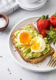 an egg and avocado toast on a plate with strawberries next to it